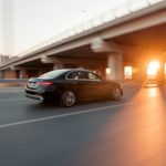 Black car drives under bridge at sunset