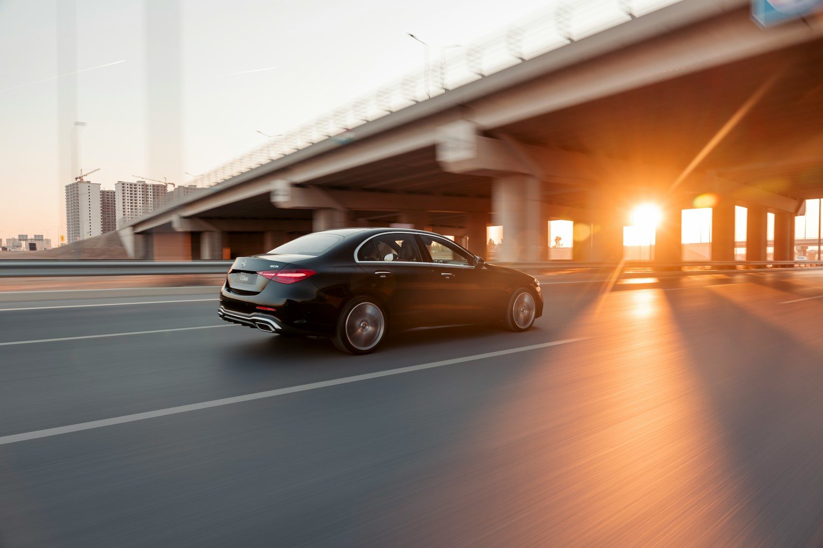 Black car drives under bridge at sunset